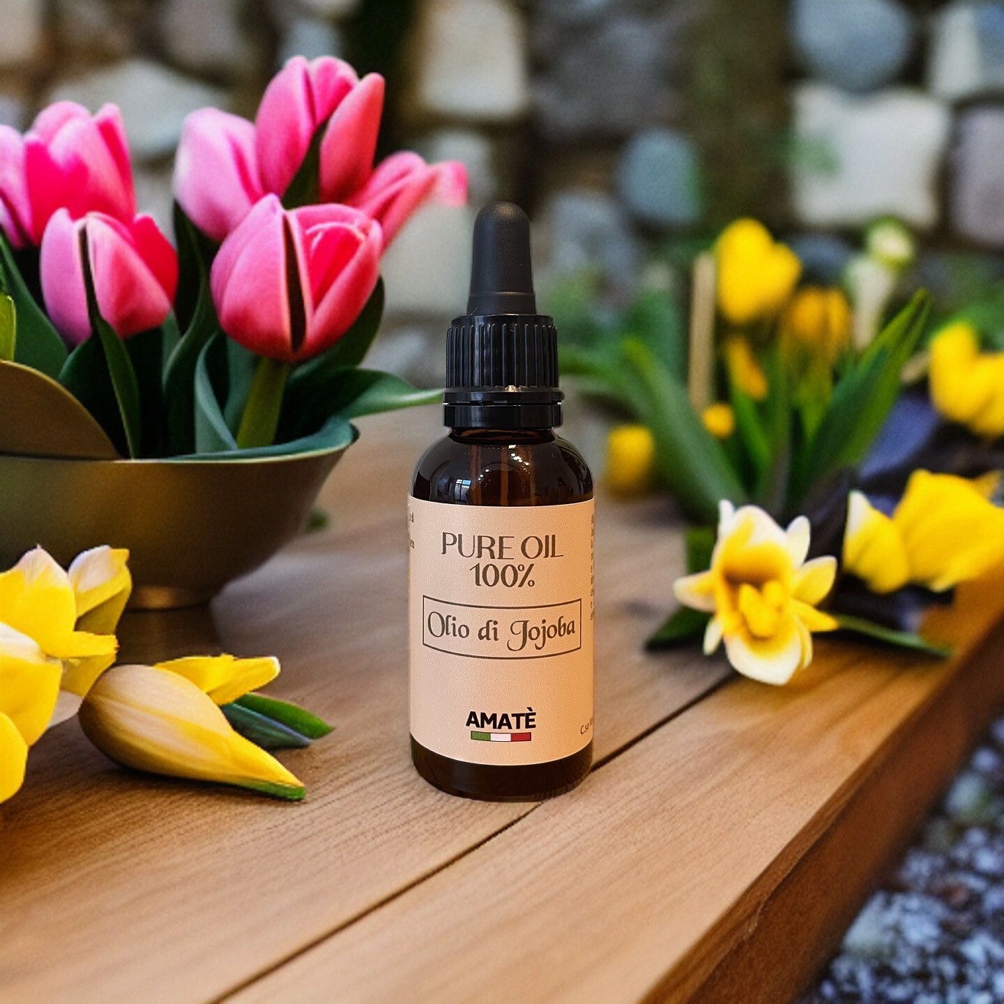 Flacone di vetro marrone con contagocce nero su legno. Etichetta "PURE OIL 100%" e "Olio di Jojoba". Marchio: AMATÈ. Fiori sullo sfondo.