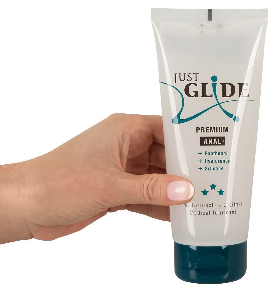 Mano che tiene un tubo di gel lubrificante Just Glide Premium Anal. Contenitore trasparente con tappo blu.