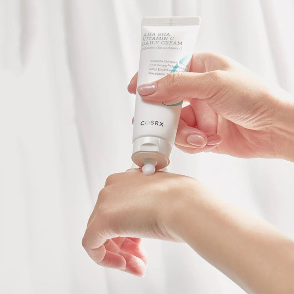 Mani che tengono un tubo AHA BHA Vitamin C Daily Cream. Crema spremuta sulla mano.