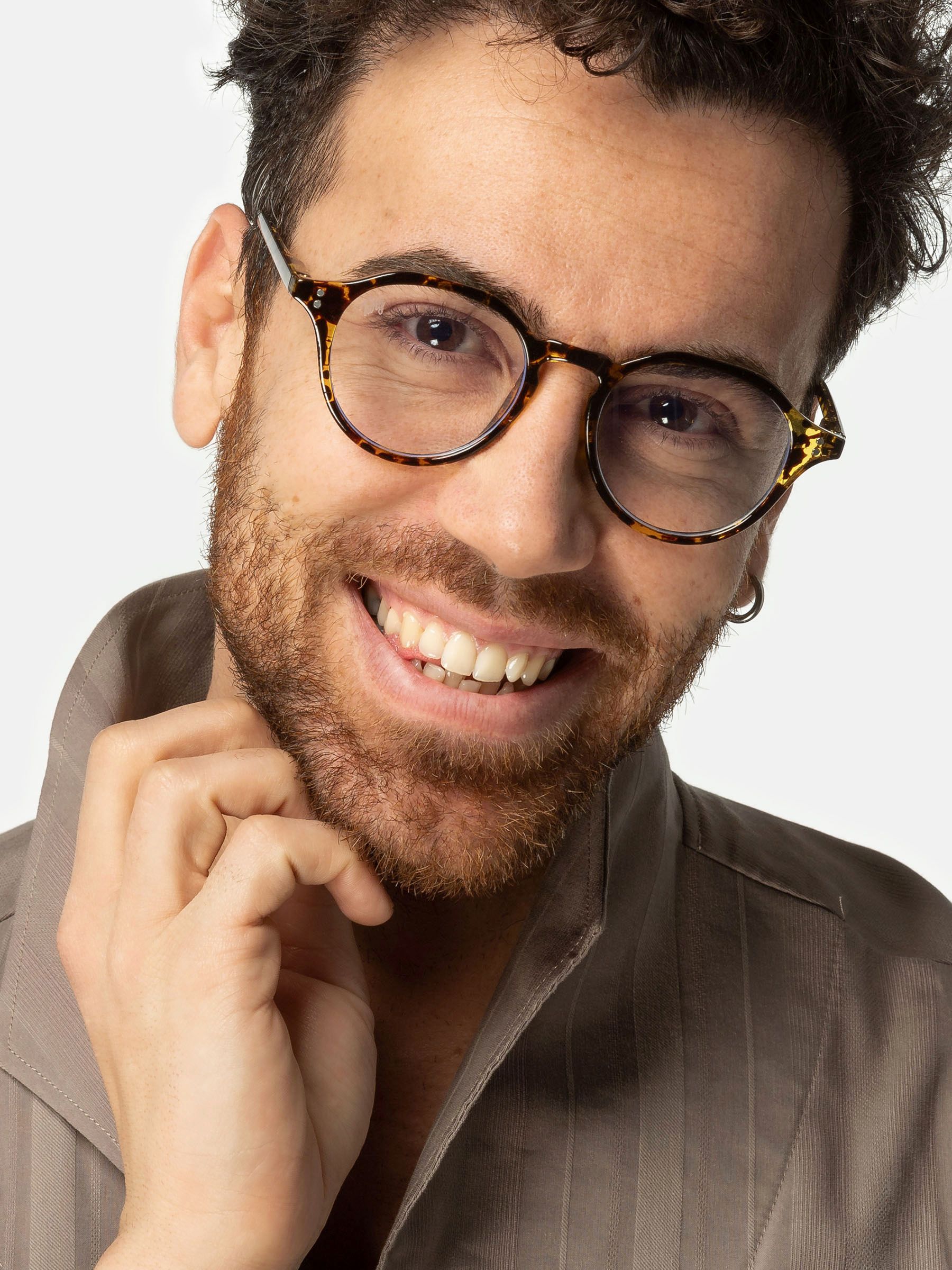 Uomo con occhiali. Lenti rotonde, motivo leopardato marrone. Sorride. Camicia beige.