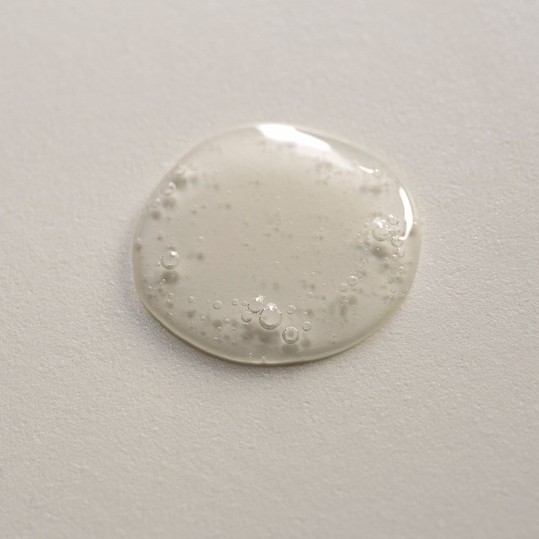 Goccia di sapone liquido trasparente con bollicine su superficie chiara.