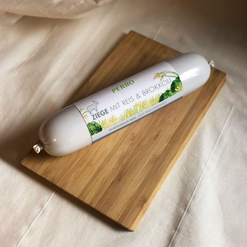 Salsiccia su tagliere di legno. Etichetta: PERRO, ZIEGE MIT REIS & BROKKOLI. Prodotto per cani.