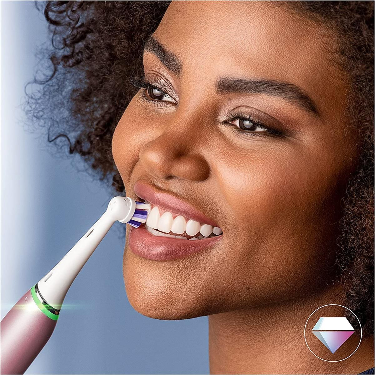 Donna che si lava i denti con uno spazzolino iO. Manico rosa, setole viola e blu. Simbolo diamante.