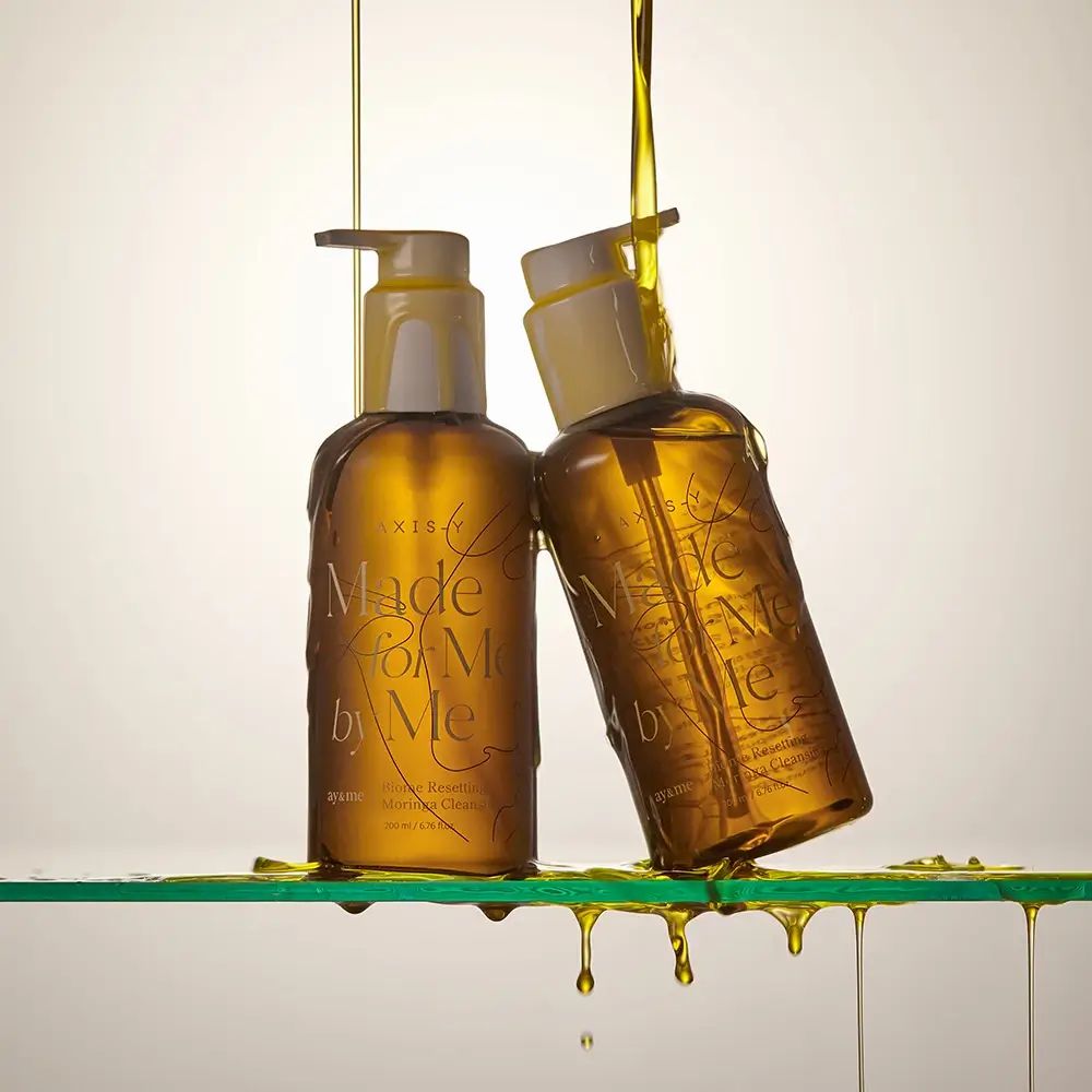Due flaconi marroni con colata d'olio. Scritta: AXIS-Y, Made for Me by Me, Biome Resetting Moringa Cleansing Oil.