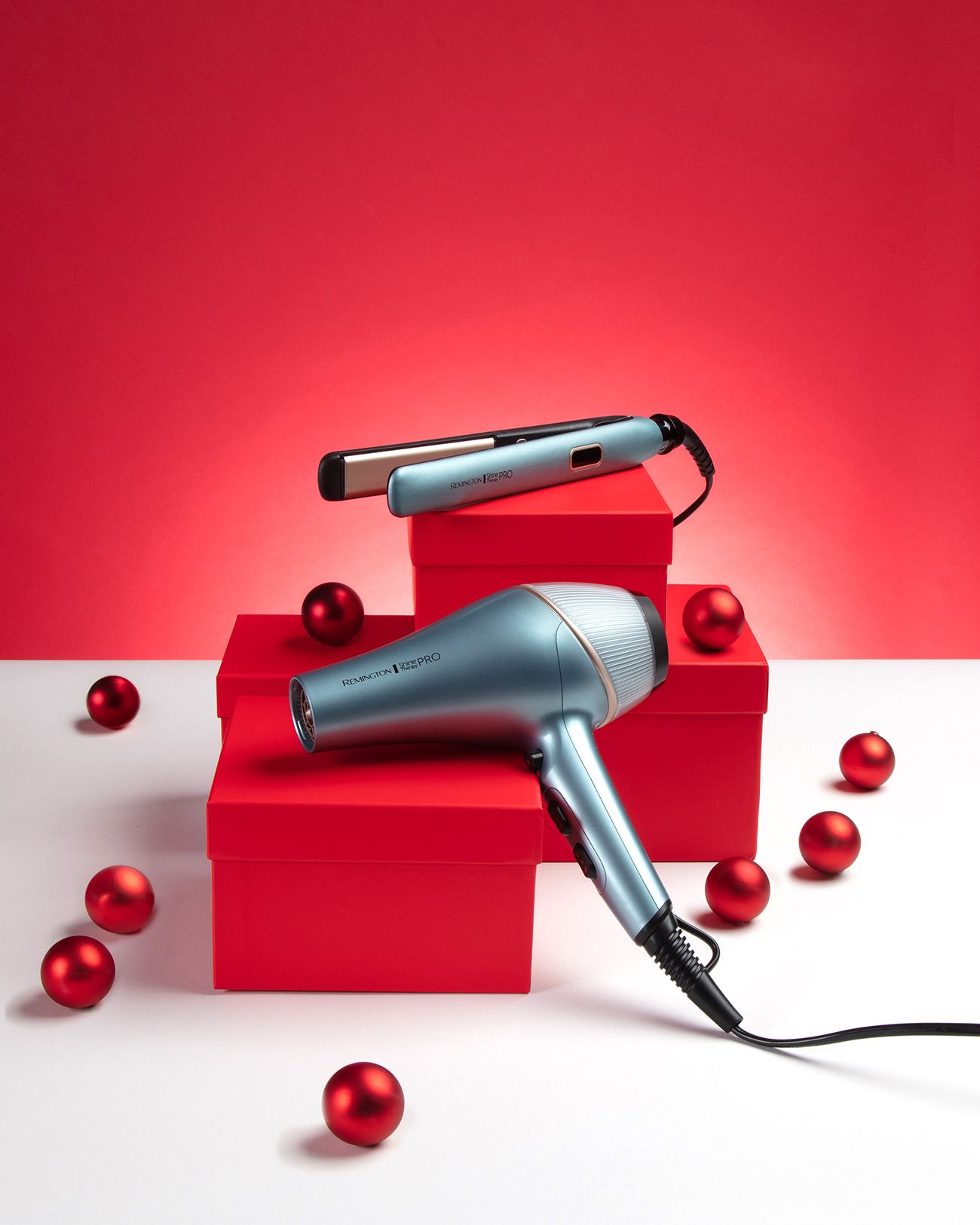 Asciugacapelli e piastra Remington turchesi su scatole regalo rosse, decorati con palline rosse.