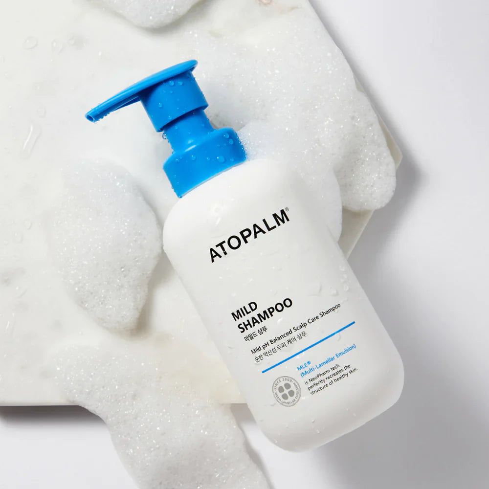 Flacone bianco con erogatore blu, circondato da schiuma. Scritta: ATOPALM, MILD SHAMPOO.
