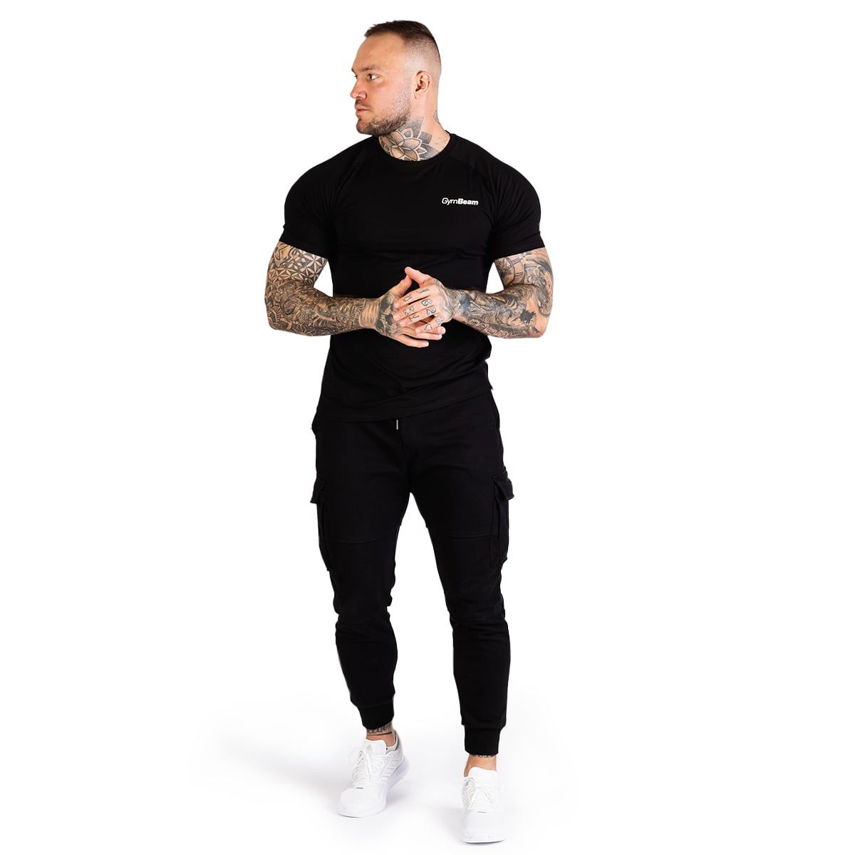 Uomo con t-shirt nera GymBeam e pantaloni cargo, in piedi frontalmente, mani in tasca.