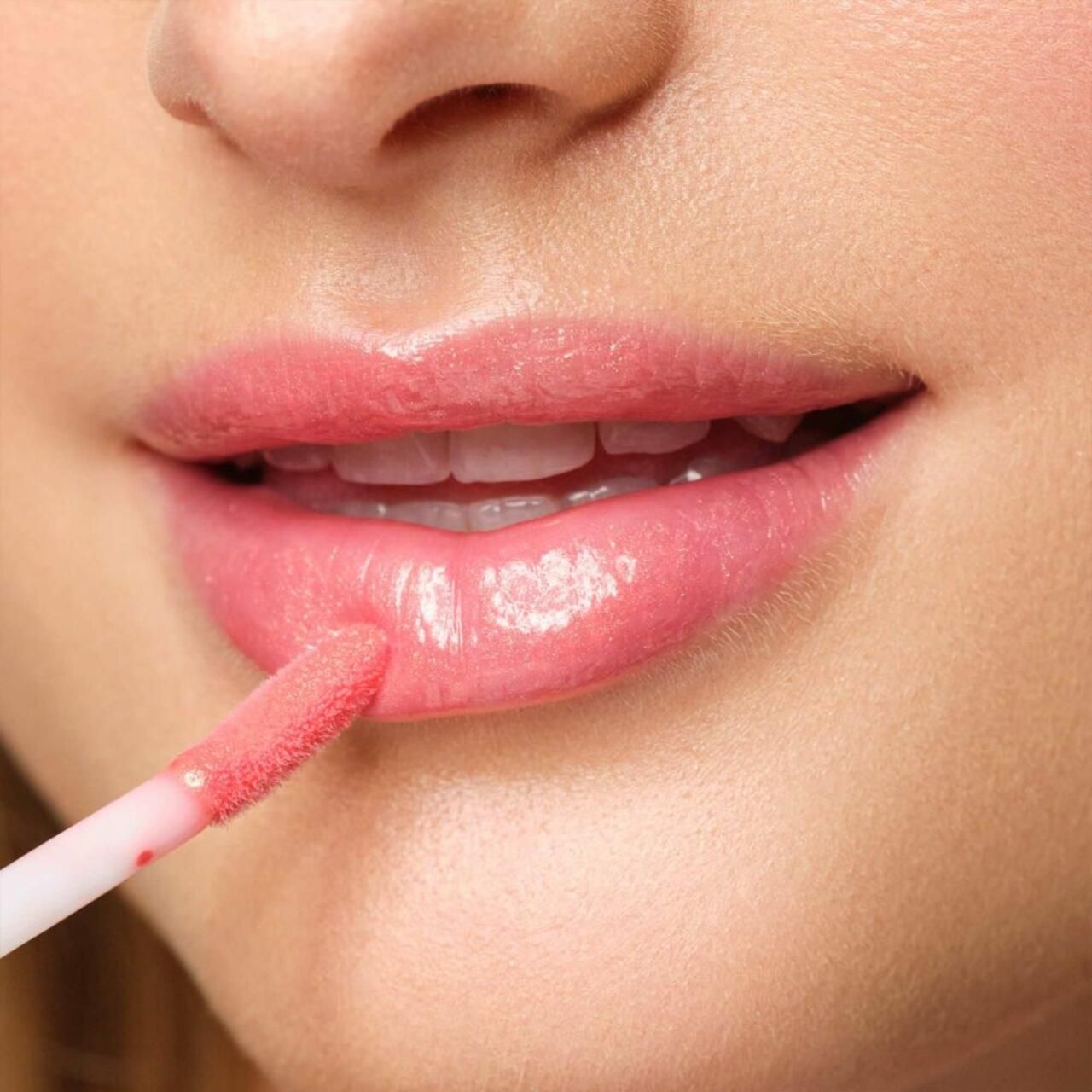 Primo piano di labbra rivestite di Lip Fluid rosa. Applicatore in uso.