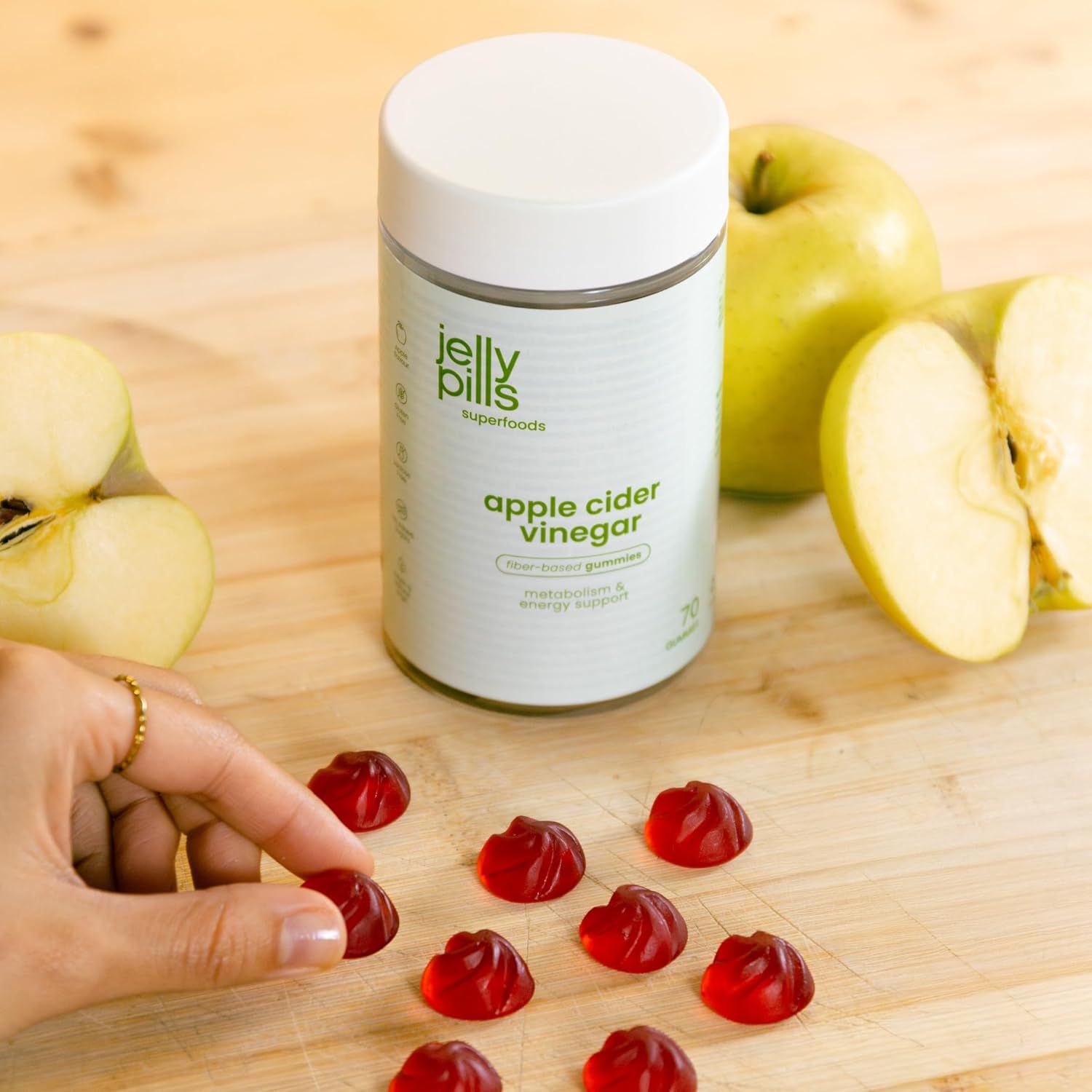 Persona prende caramelle gommose da un tagliere. Barattolo e mele sullo sfondo.
