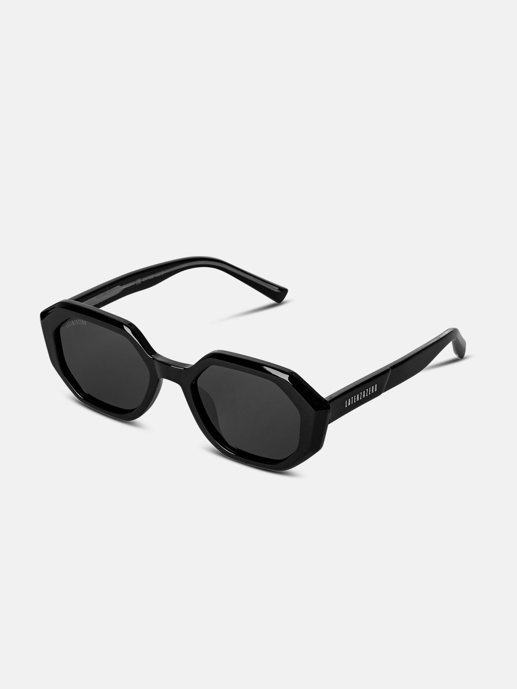 Occhiali da sole neri con lenti ottagonali. La montatura è anch'essa nera. Il nome del marchio è visibile sull'asta.