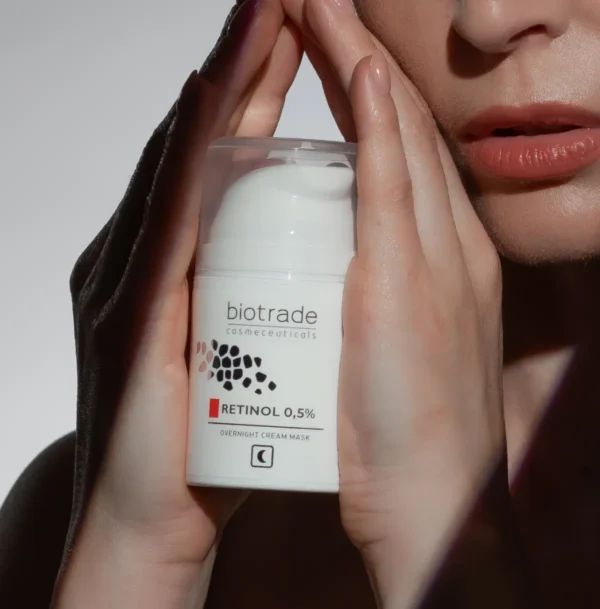 Flacone bianco con scritta Biotrade, Retinolo 0,5%. Mani che tengono il flacone. Maschera notte.