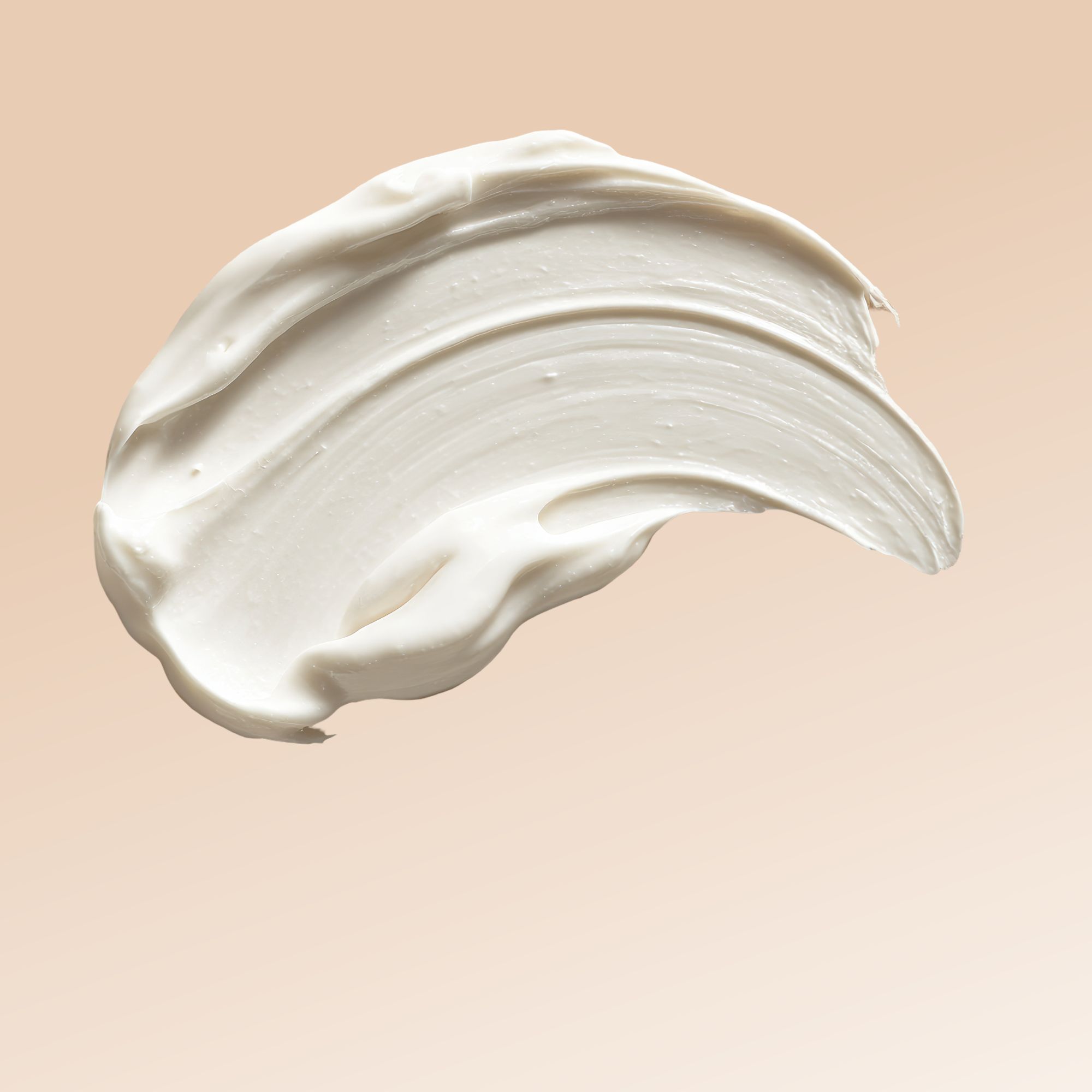 Primo piano di una striscia di crema color crema su sfondo beige. La crema è densa e strutturata.