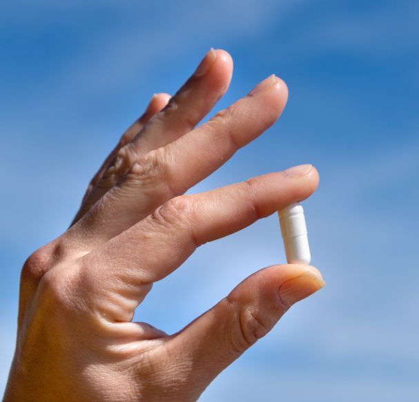 Mano che tiene una capsula bianca di Aavalabs Magnesium Komplex.