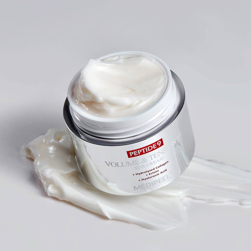 Contenitore di crema aperto con corpo argentato, riempito di crema bianca. Crema sparsa sulla superficie.