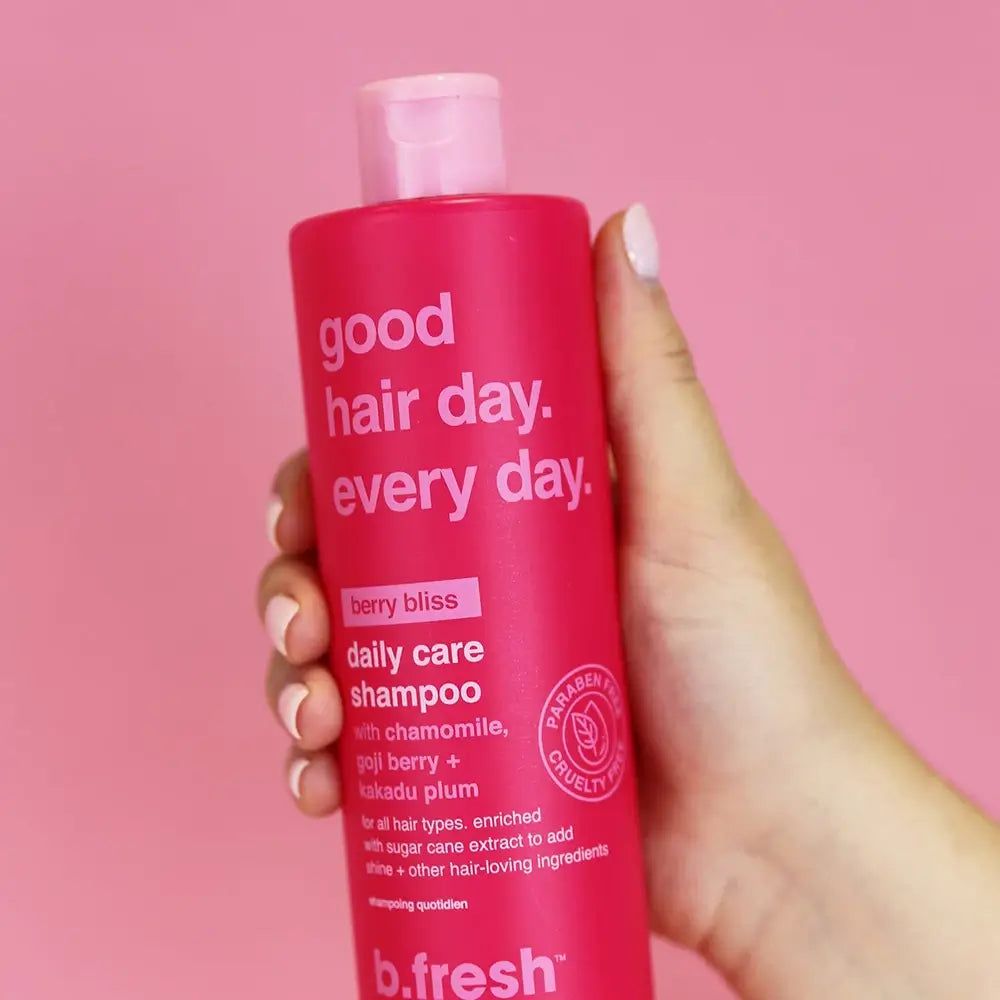 Flacone di shampoo rosso tenuto in mano. Scritta: good hair day. every day. berry bliss daily care shampoo. b.fresh.
