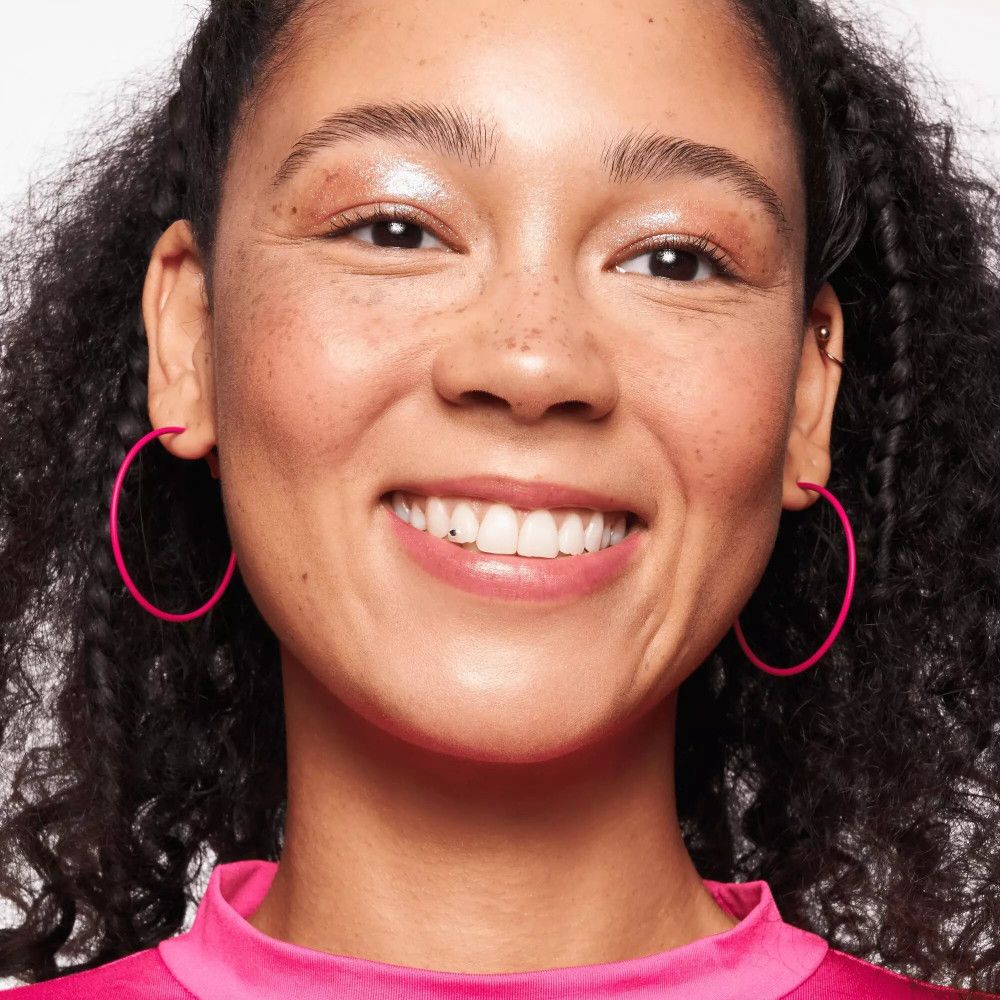 Primo piano di una donna con orecchini rosa. Ha lentiggini e indossa trucco.