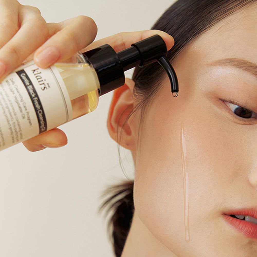 Persona che tiene in mano un flacone di Gentle Black Fresh Cleansing Oil. L'olio viene applicato sulla pelle. Primo piano del viso.