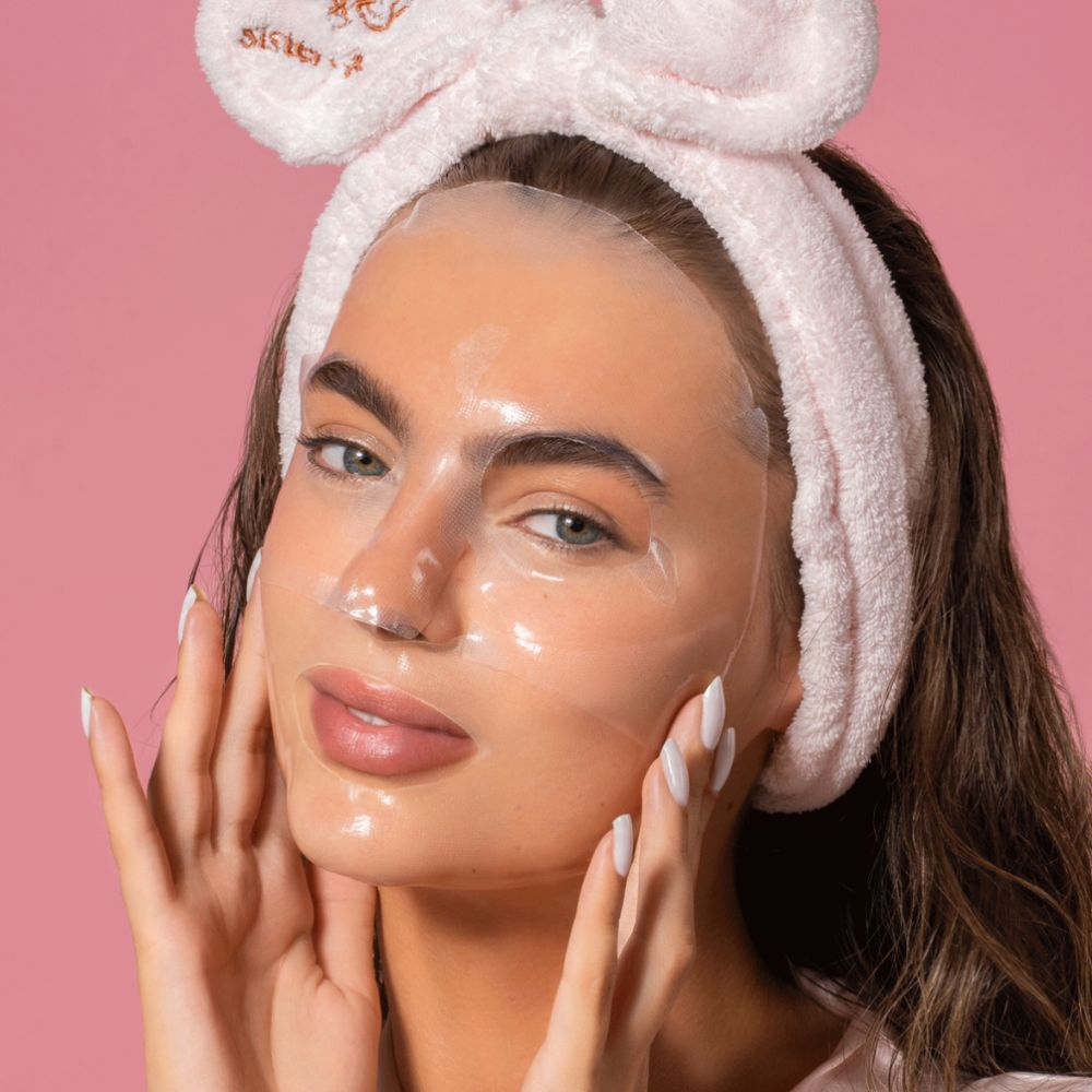 Donna con maschera viso. Sfondo rosa. La donna tocca la maschera con le mani.