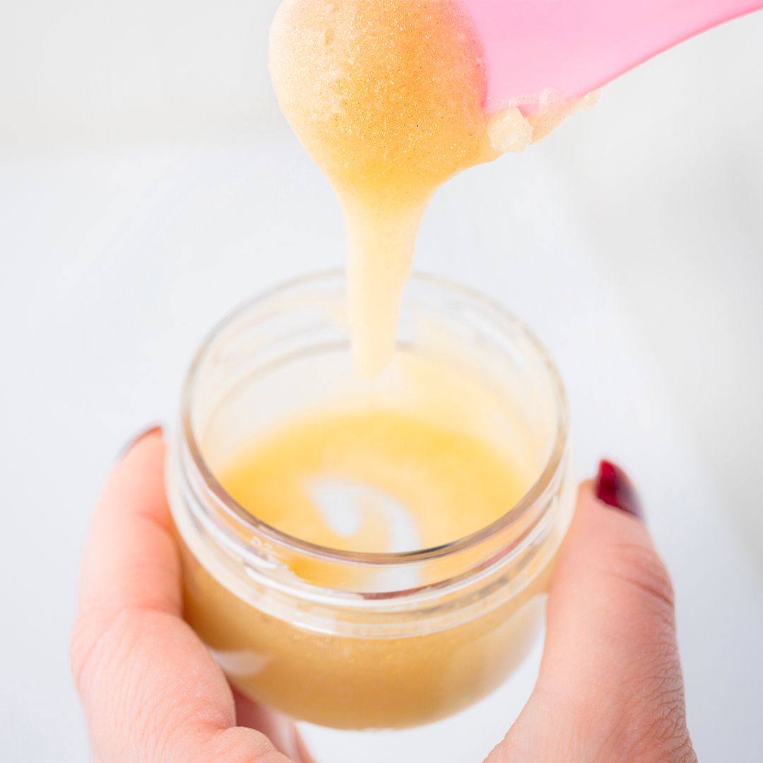 Sostanza gialla versata in un bicchiere. Spatola rosa. Contenitore di vetro. Primo piano.