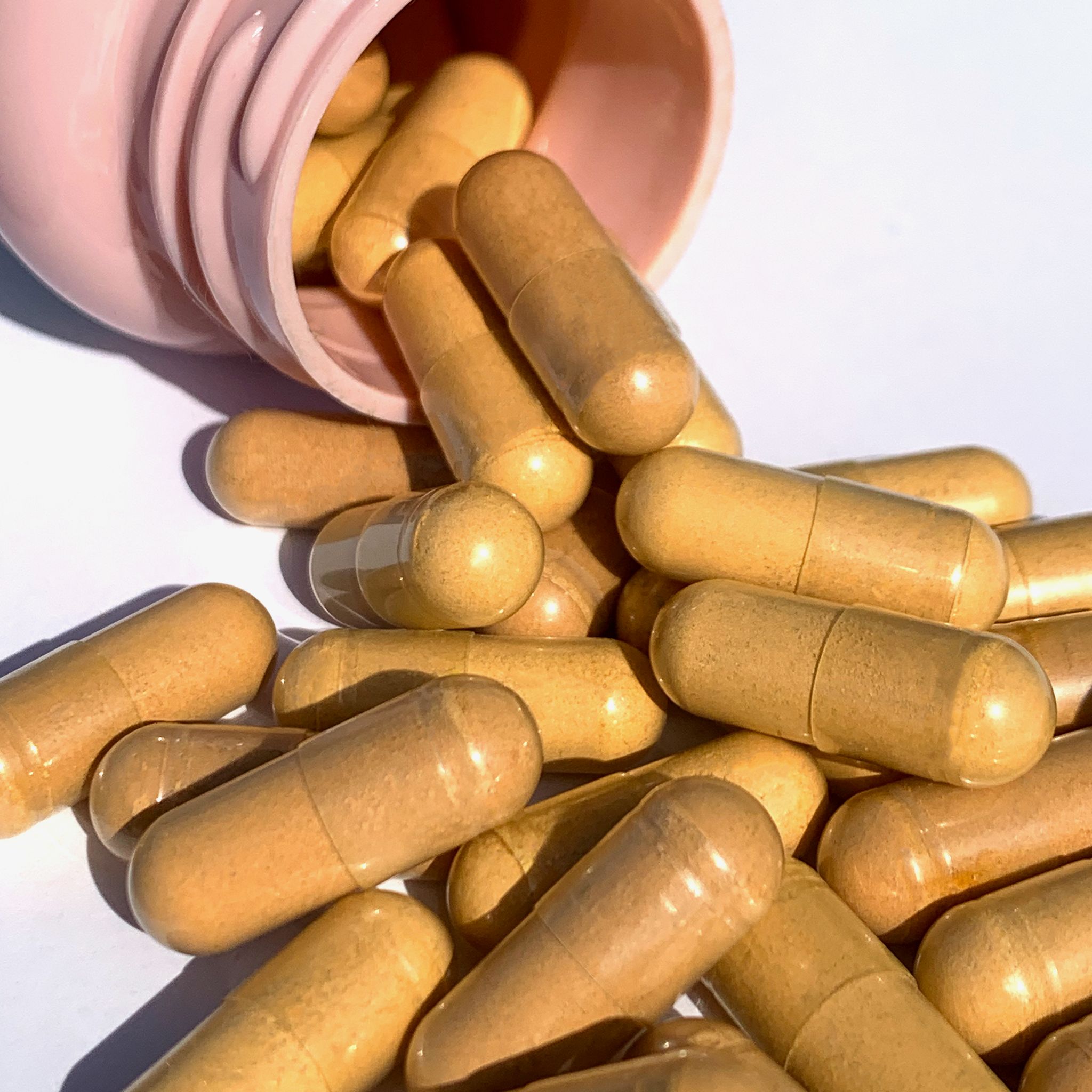 Mucchio di capsule marroni che cadono da un flacone rosa. Primo piano.