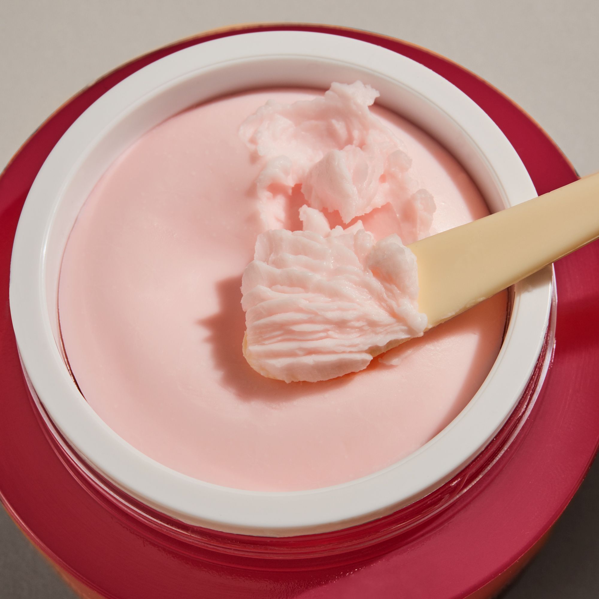 Vaso di crema rosa aperto con crema e spatola. Consistenza della crema visibile.
