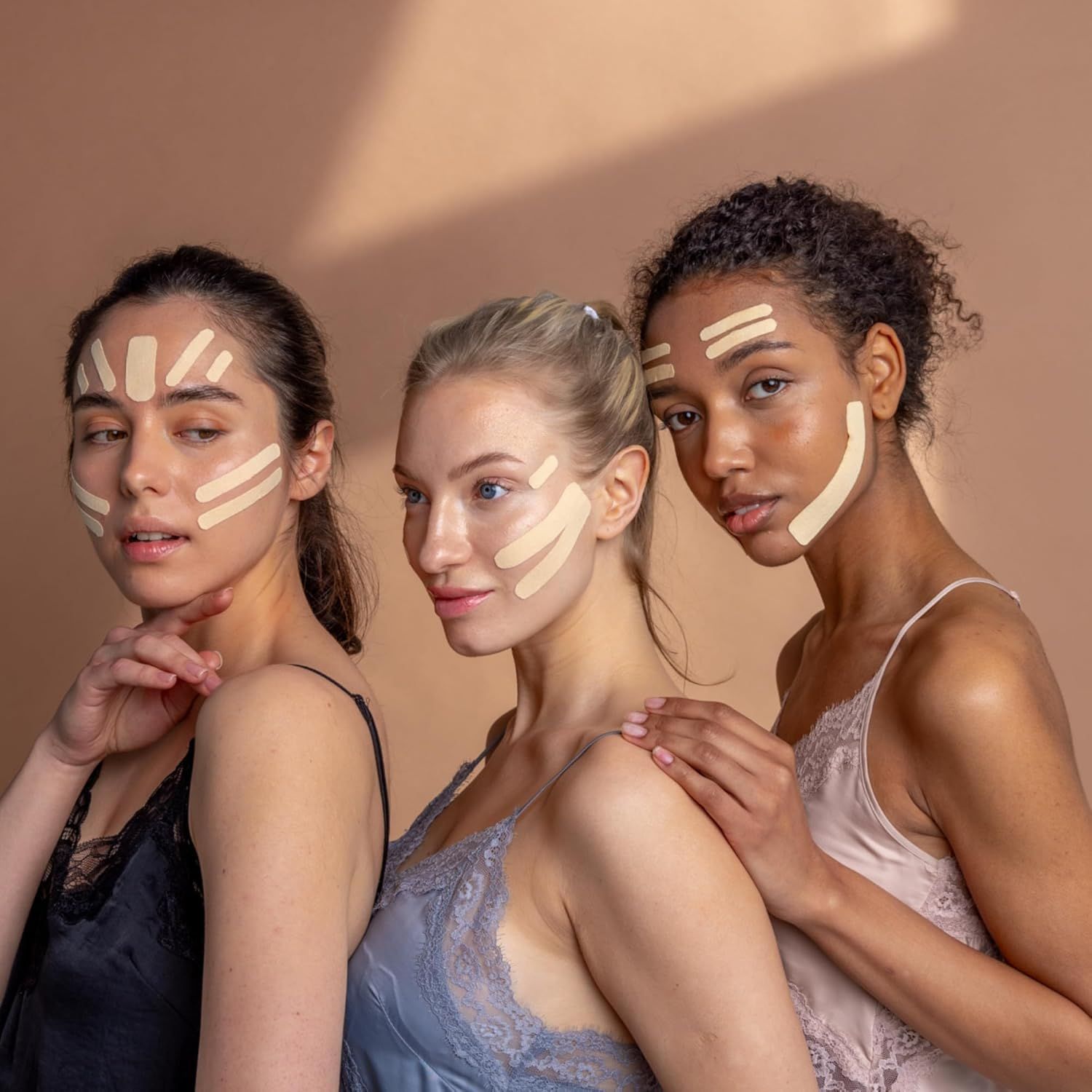 Tre donne con strisce di tape sul viso. Diverse tonalità di pelle. Indossano top.