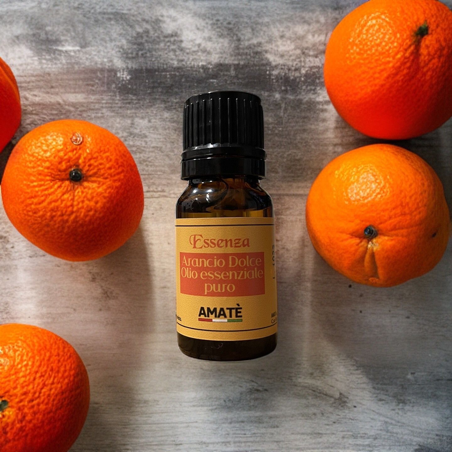 Flacone di vetro marrone con tappo nero, circondato da arance. Etichetta con testo: Arancio Dolce, Olio essenziale puro, AMATÈ.