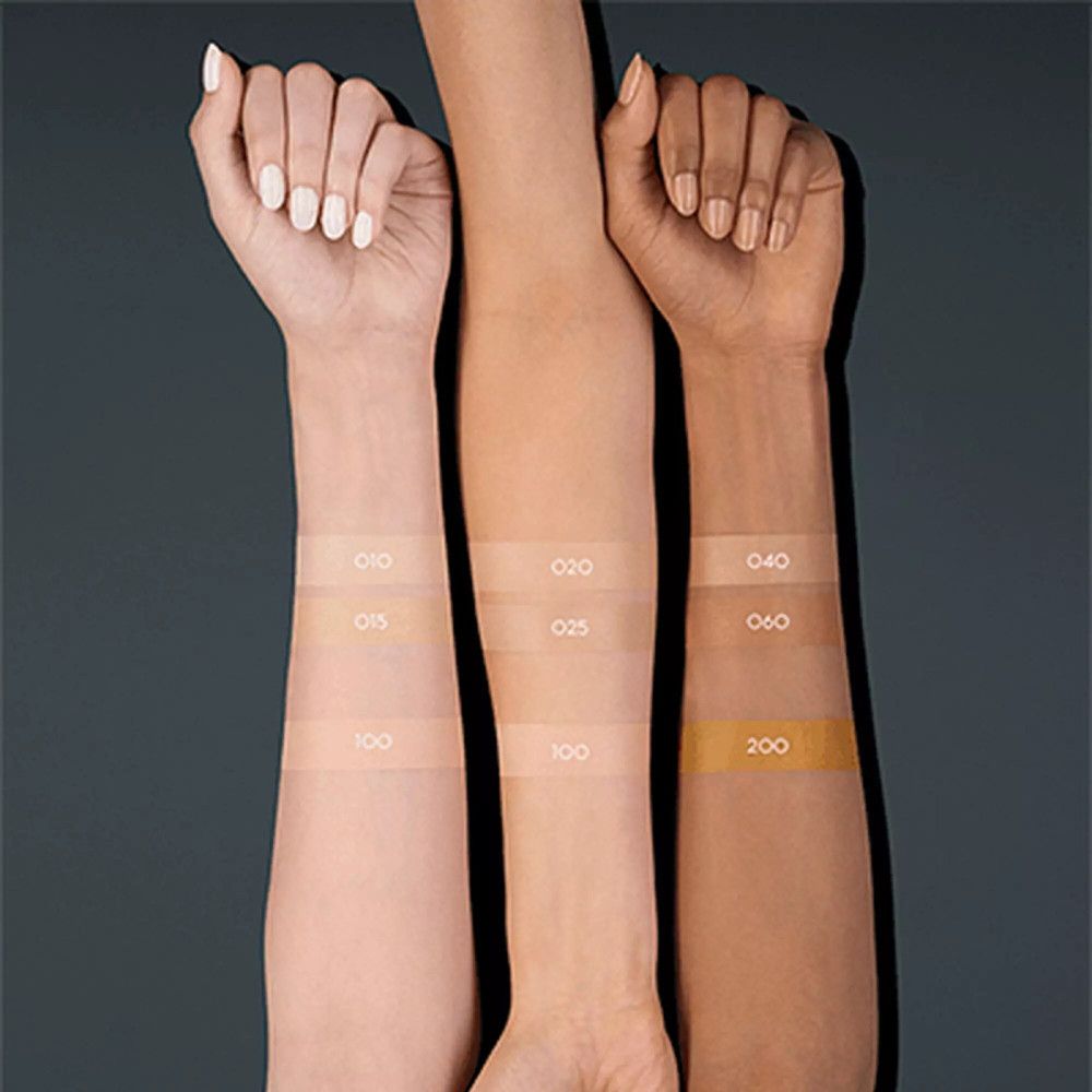 Tre braccia con diverse tonalità di pelle, su cui sono applicati i colori della crema correttiva. I numeri dei colori sono visibili.