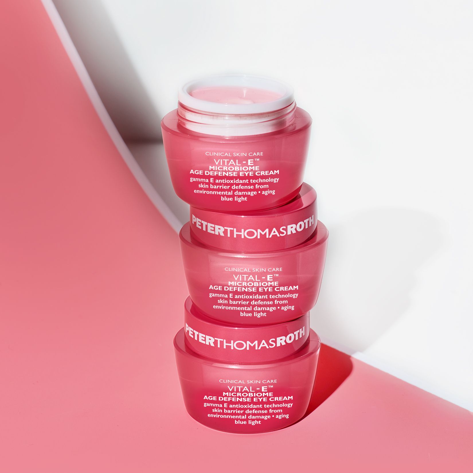 Quattro vasi rosa impilati. Testo: VITAL-E MICROBIOME AGE DEFENSE EYE CREAM. Scritta PETERTHOMASROTH. Su sfondo rosa.