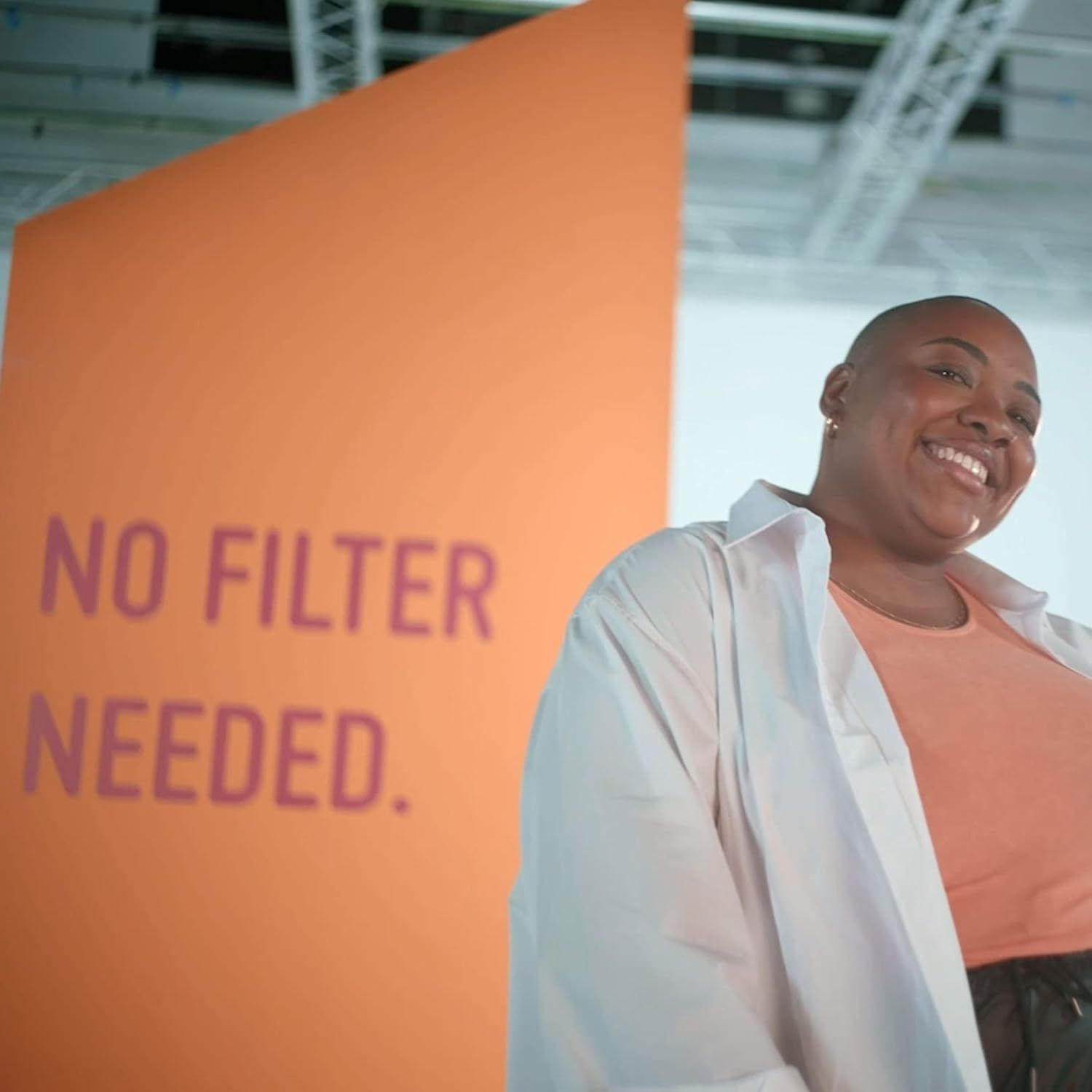 Una persona sorride davanti a uno sfondo arancione con la scritta "NO FILTER NEEDED."
