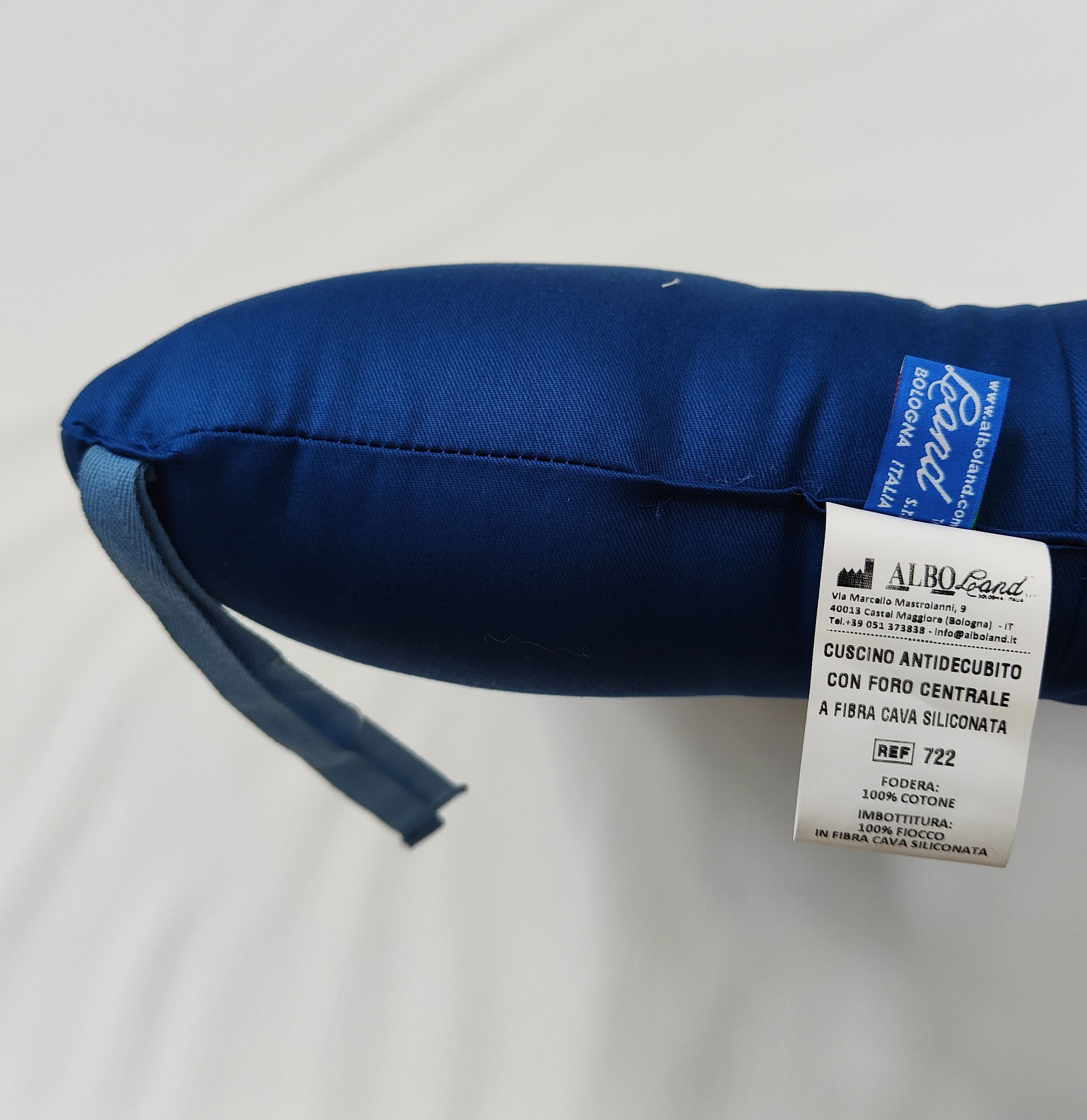 Cuscino blu con foro. Etichetta con informazioni prodotto e marchio Alboland. Nastri blu.