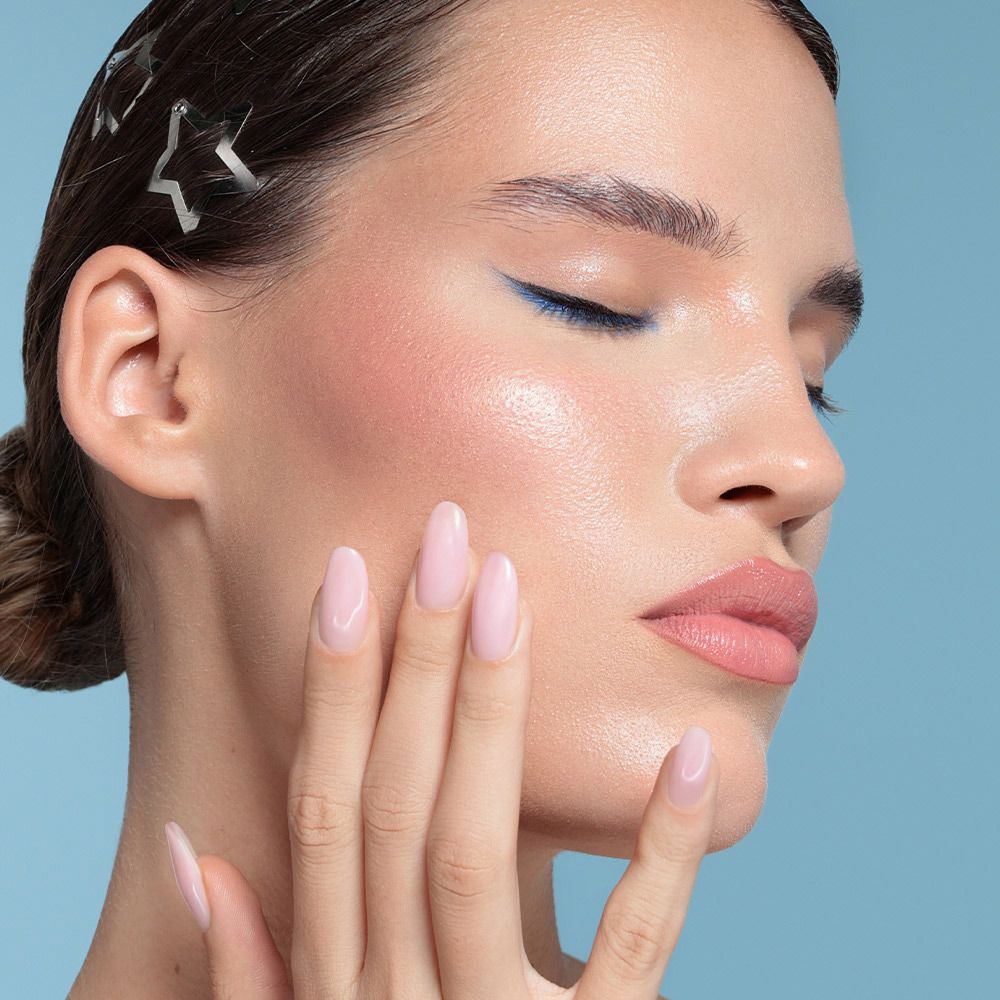 Una donna si tocca il viso. Ha un trucco occhi blu e labbra rosa. Ci sono forcine d'argento nei suoi capelli.