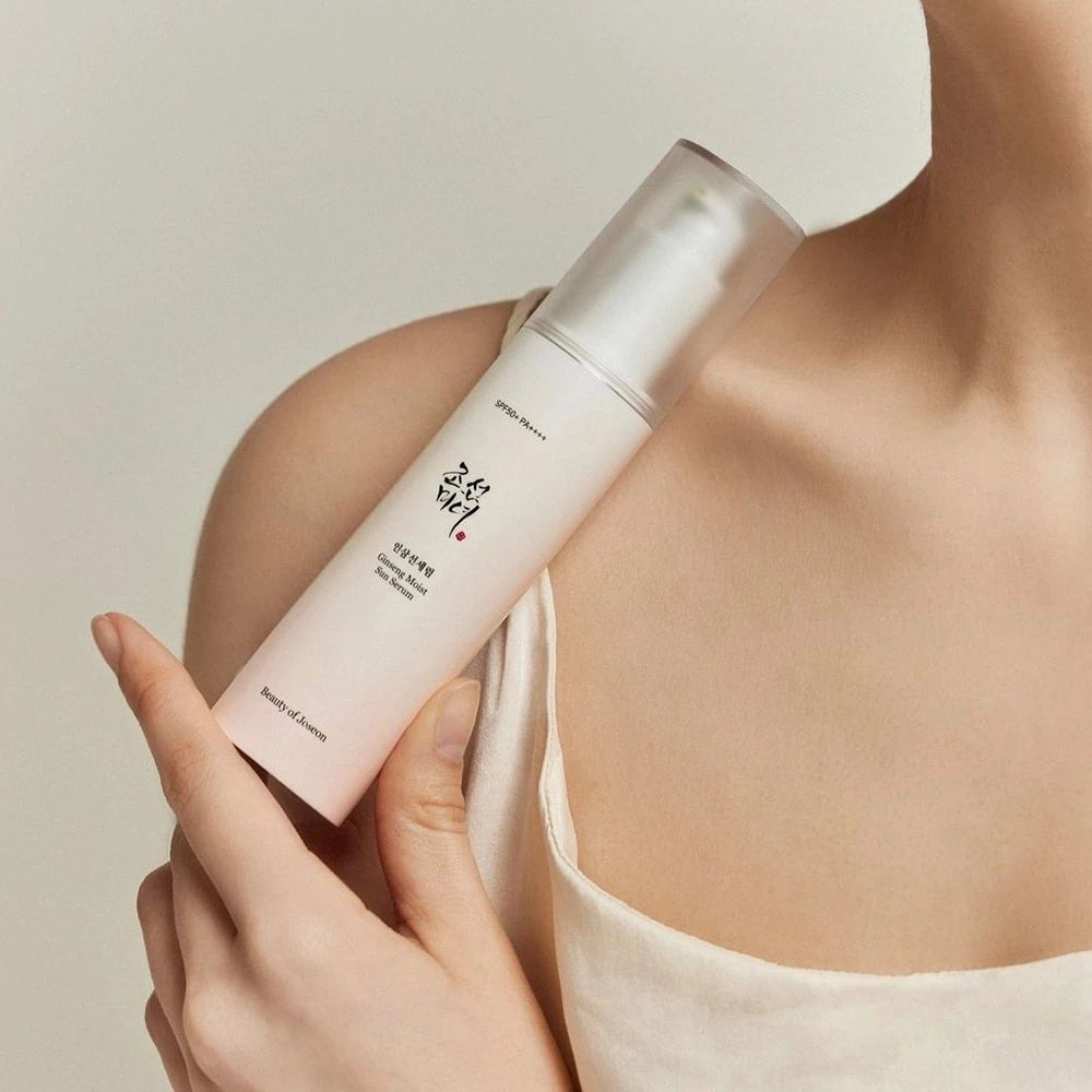 Persona che tiene in mano un flacone. Scritta: Ginseng Moist Sun Serum, SPF 50 PA++++. Marchio: Beauty of Joseon.