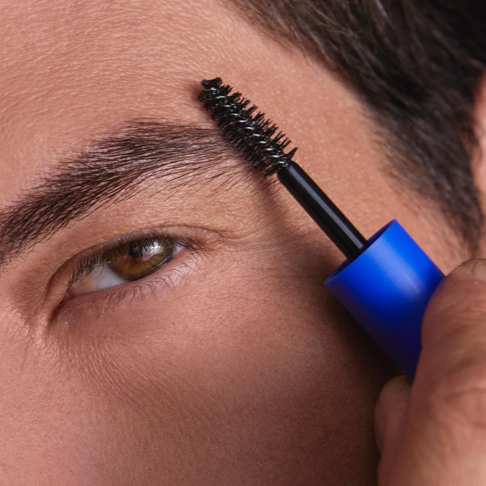 Gel per sopracciglia applicato su un sopracciglio. Spazzola nera, manico blu. Primo piano.