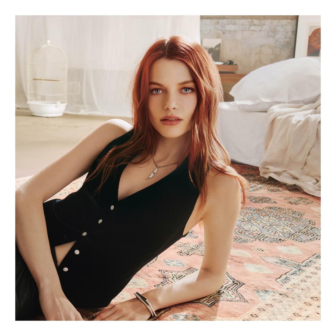 Donna con capelli rossi sdraiata su un tappeto. Indossa un gilet nero e un braccialetto.