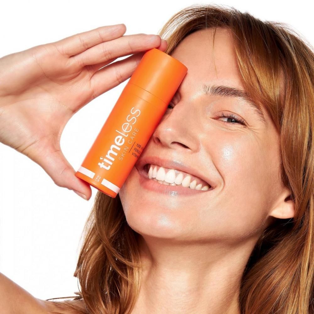 Donna tiene in mano un flacone arancione. Scritta: Timeless Skin Care. Prodotto: 10% vitamina C, acido ferulico, vitamina E.