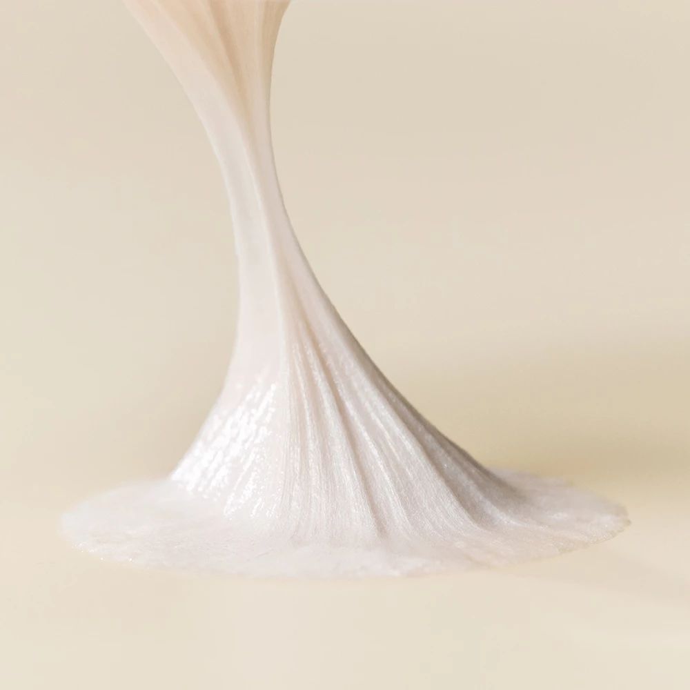 Primo piano di un filo di schiuma detergente bianca che si stende su una superficie. La schiuma ha una consistenza liscia.