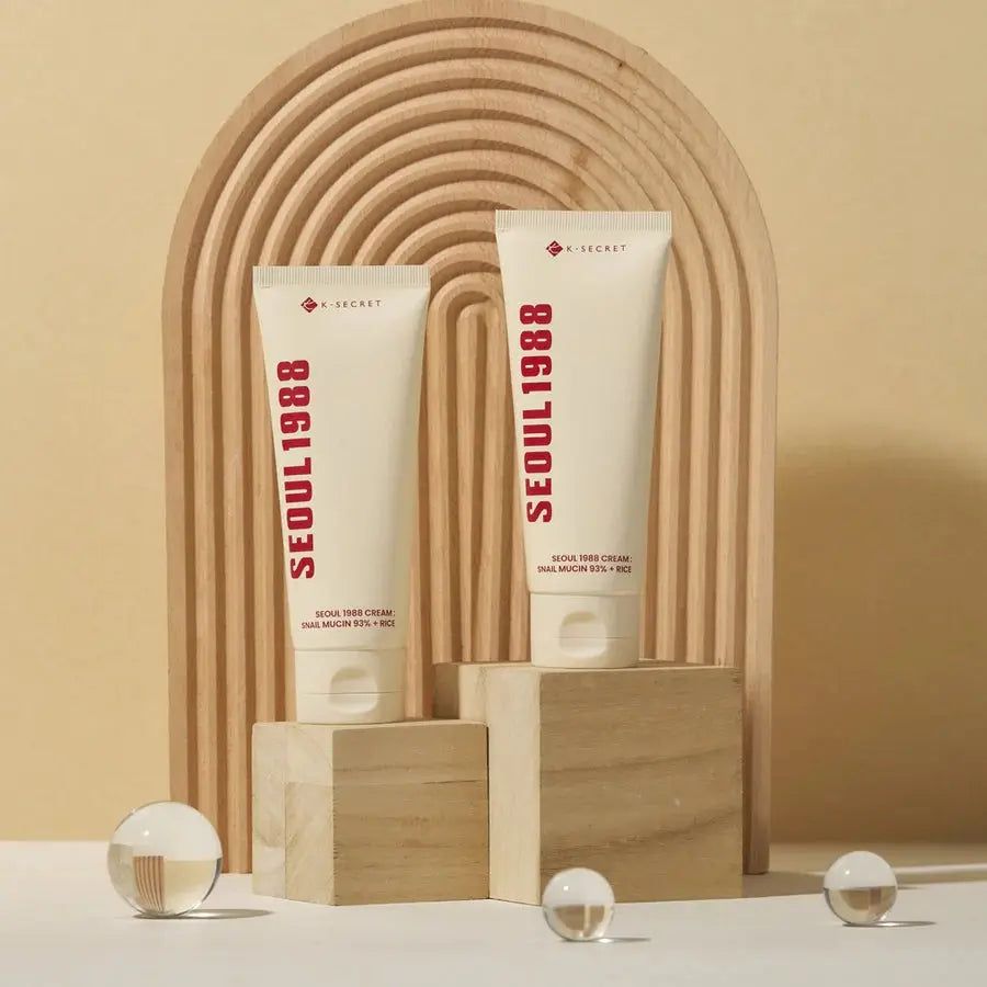 Due tubi di crema con scritta rossa SEOUL 1988. Testo: SEOUL 1988 CREAM: SNAIL MUCIN 93% + RICE. Marchio: K-SECRET.