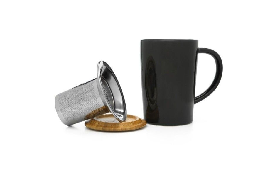 Tazza nera con manico, accanto a un colino da tè e un coperchio in legno. Su sfondo bianco.