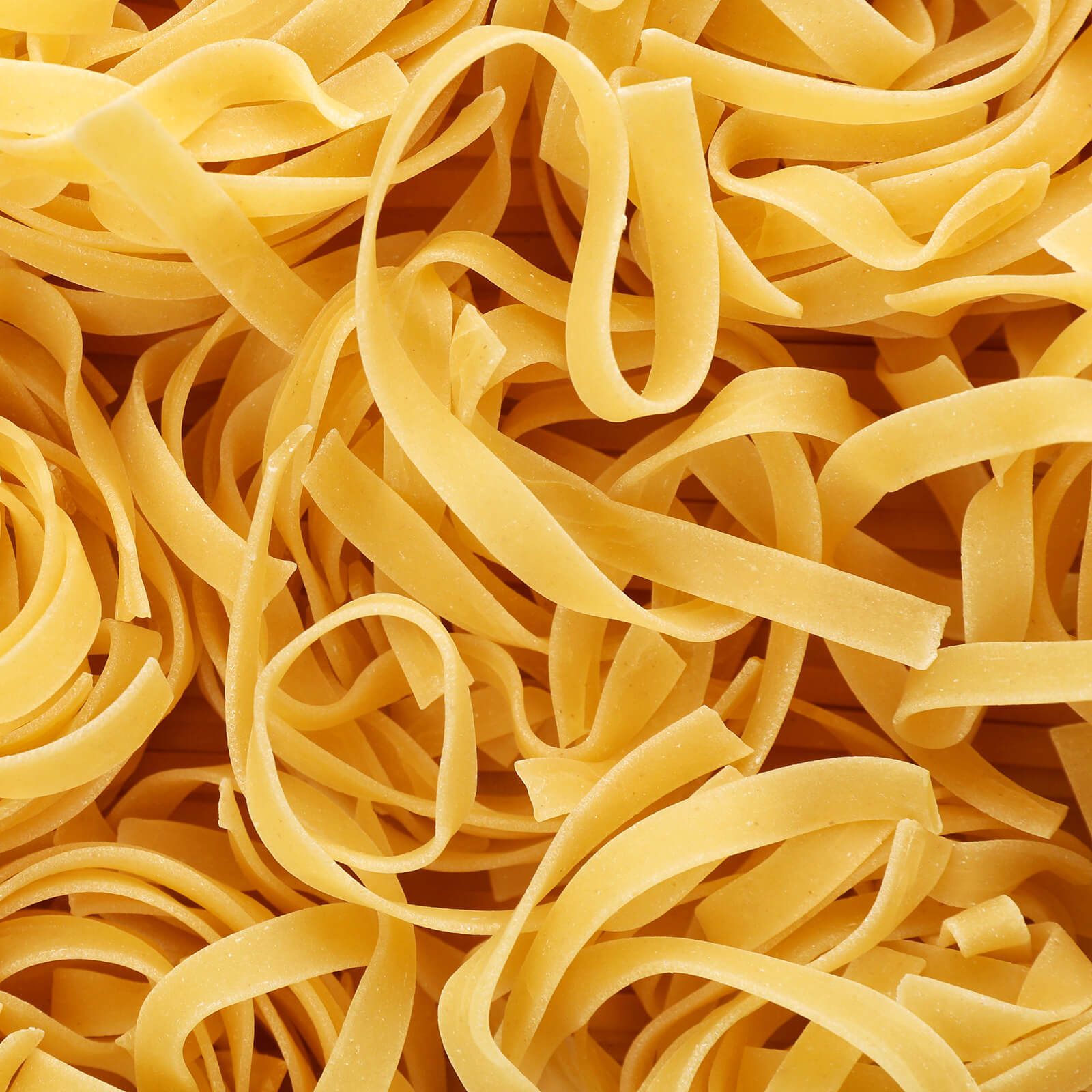 Primo piano di tagliatelle crude. Pasta piatta gialla intrecciata.