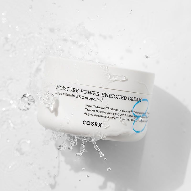 Vaso di crema bianco con acqua. Scritta: MOISTURE POWER ENRICHED CREAM, COSRX. L'acqua schizza.