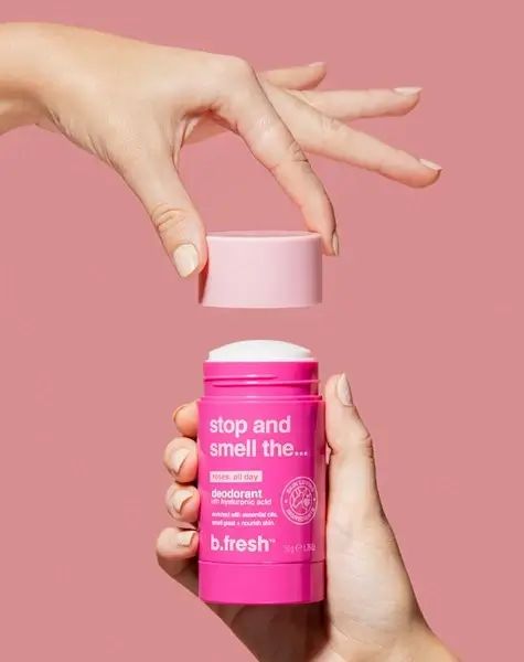 Stick deodorante rosa aperto, tenuto da mani. Confezione rosa, testa deodorante bianca. Testo: B.fresh, Stop and smell the...