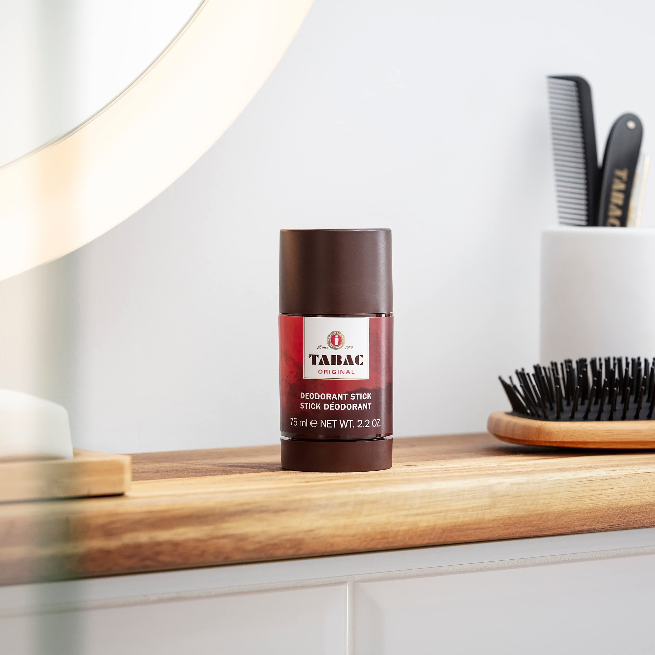 Stick deodorante su superficie in legno. Specchio, pettine e spazzola sullo sfondo. Testo: TABAC ORIGINAL.