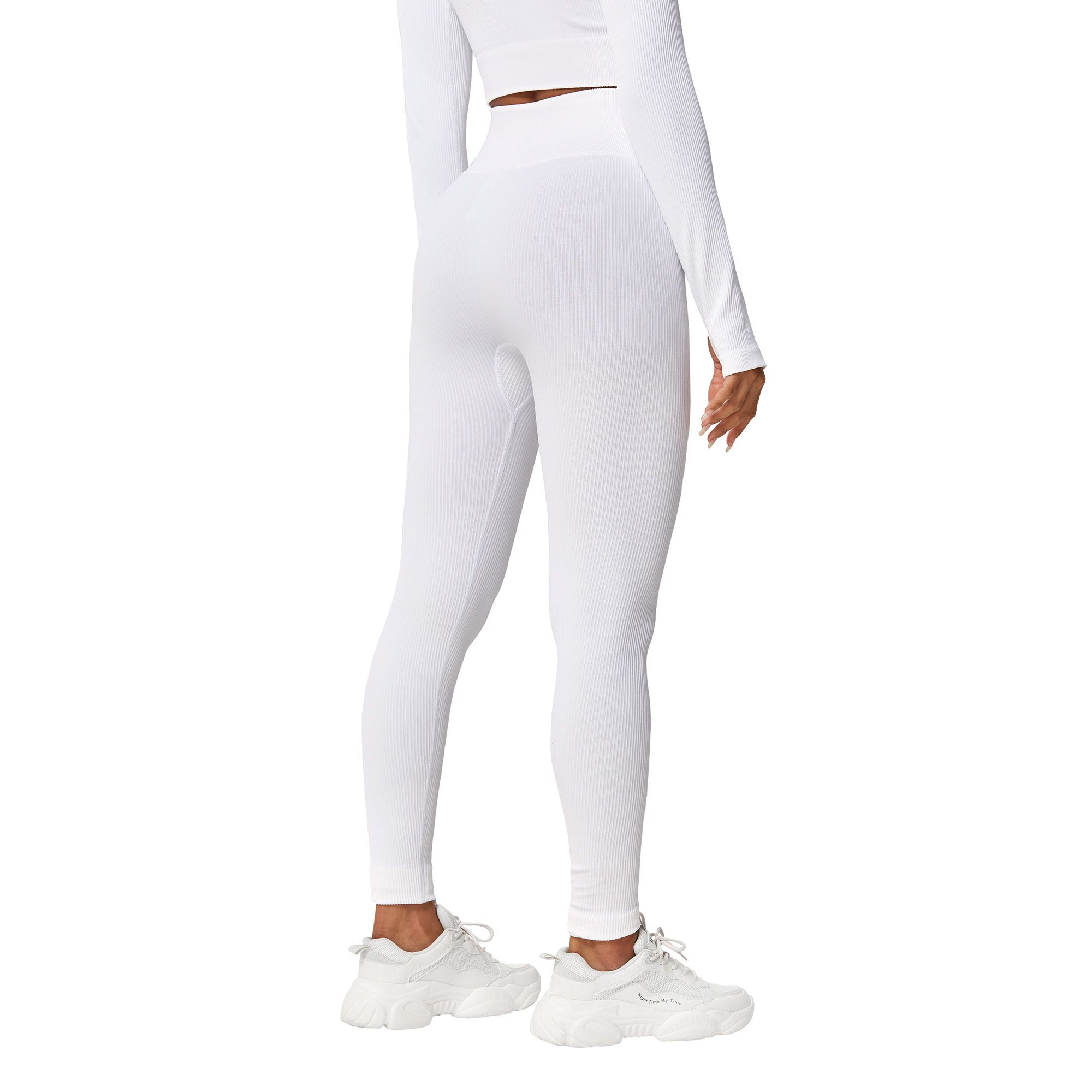 Leggings bianchi senza cuciture e maglia a maniche lunghe in materiale elasticizzato, indossati con scarpe da ginnastica bianche.