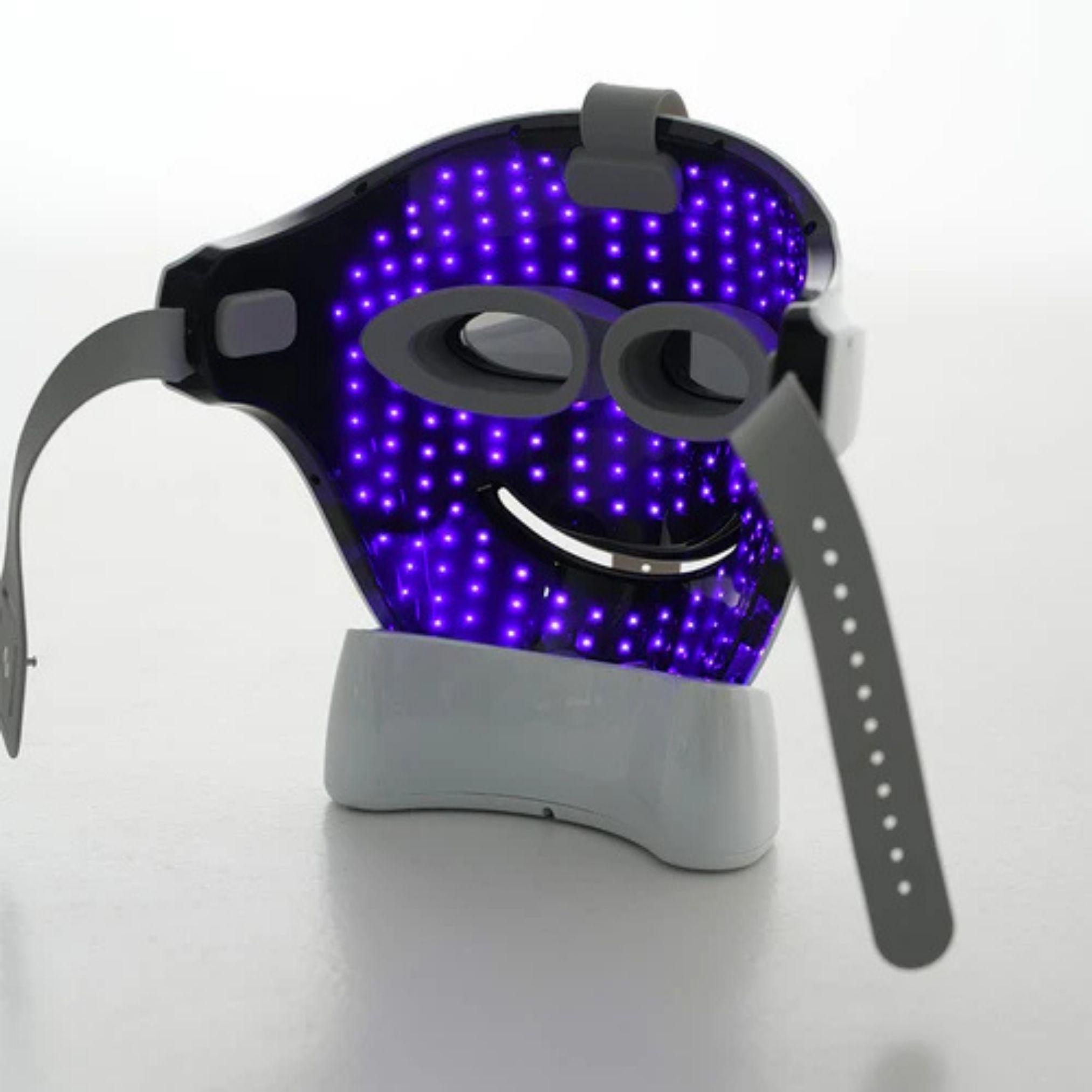Maschera facciale con LED viola. Cinghie e supporto grigi. Maschera su base bianca.