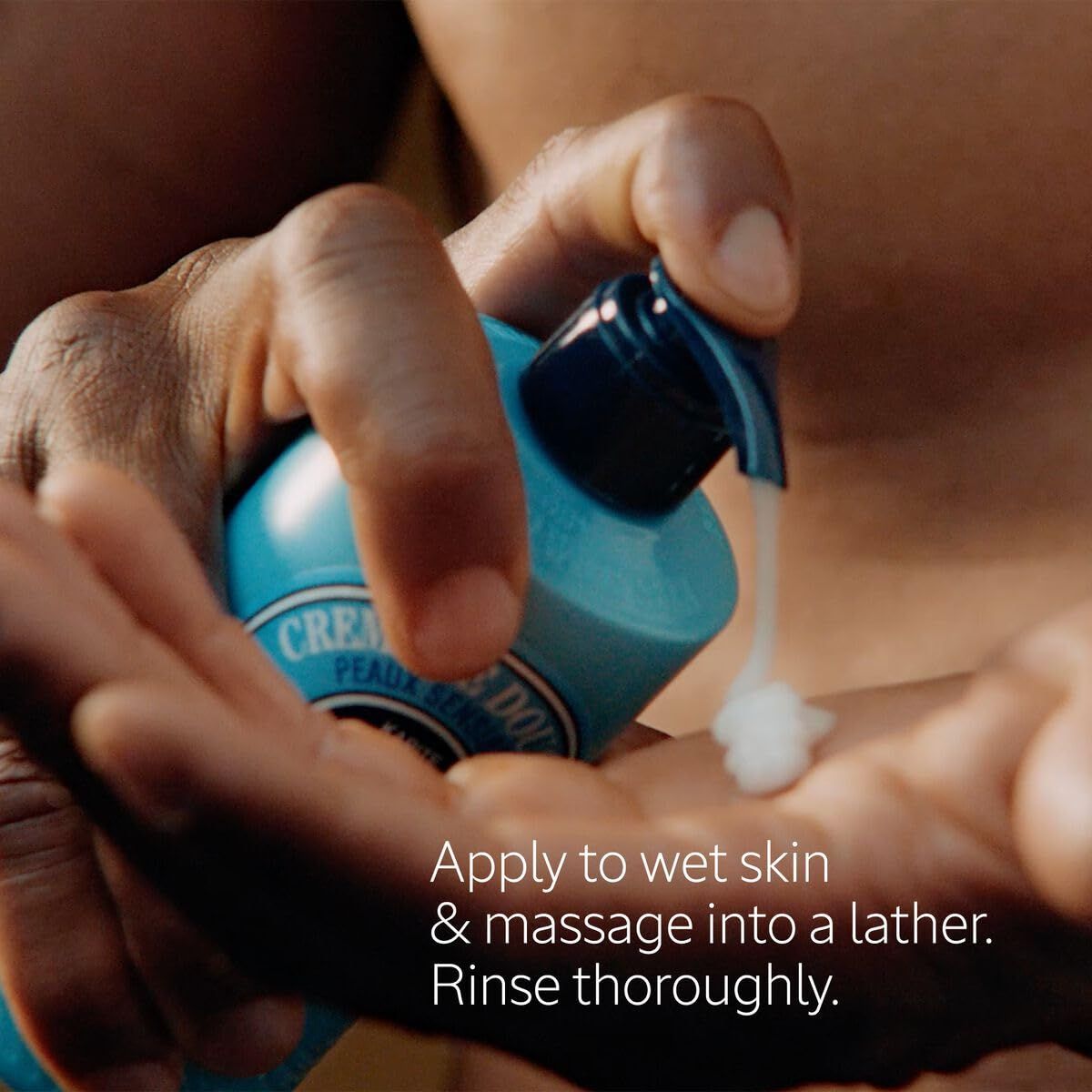 Mani che premono la crema da un flacone azzurro con dosatore. Testo: Applicare sulla pelle bagnata e massaggiare.
