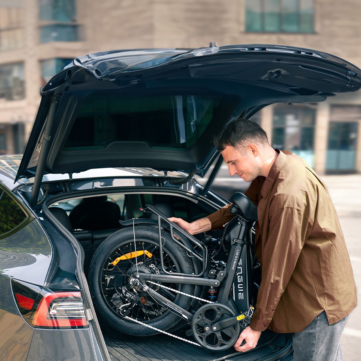 Un uomo estrae una bicicletta elettrica nera piegata da un'auto. Il logo ENGWE è visibile.
