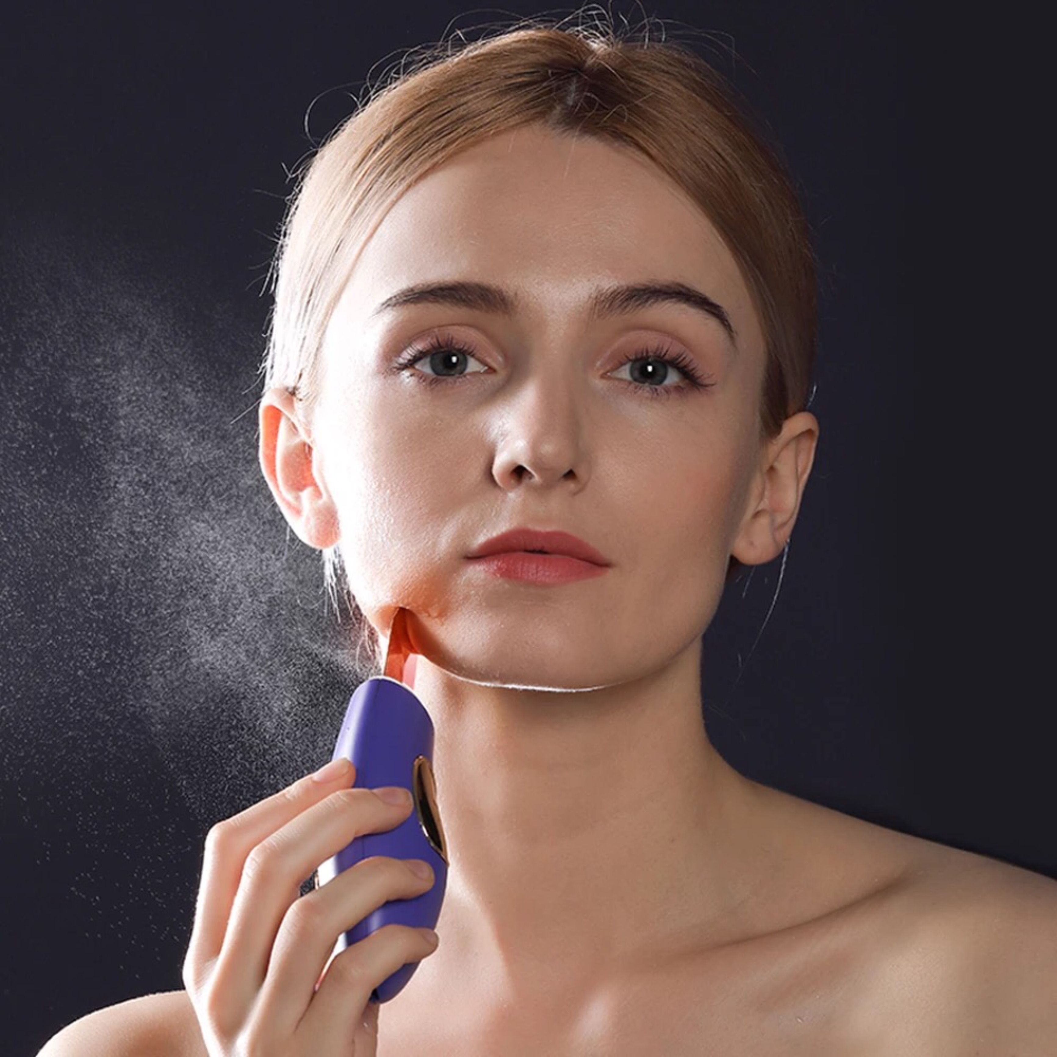 Persona che utilizza il dispositivo di peeling a ultrasuoni. Dispositivo con spatola dorata e corpo viola. Nebbia spray.