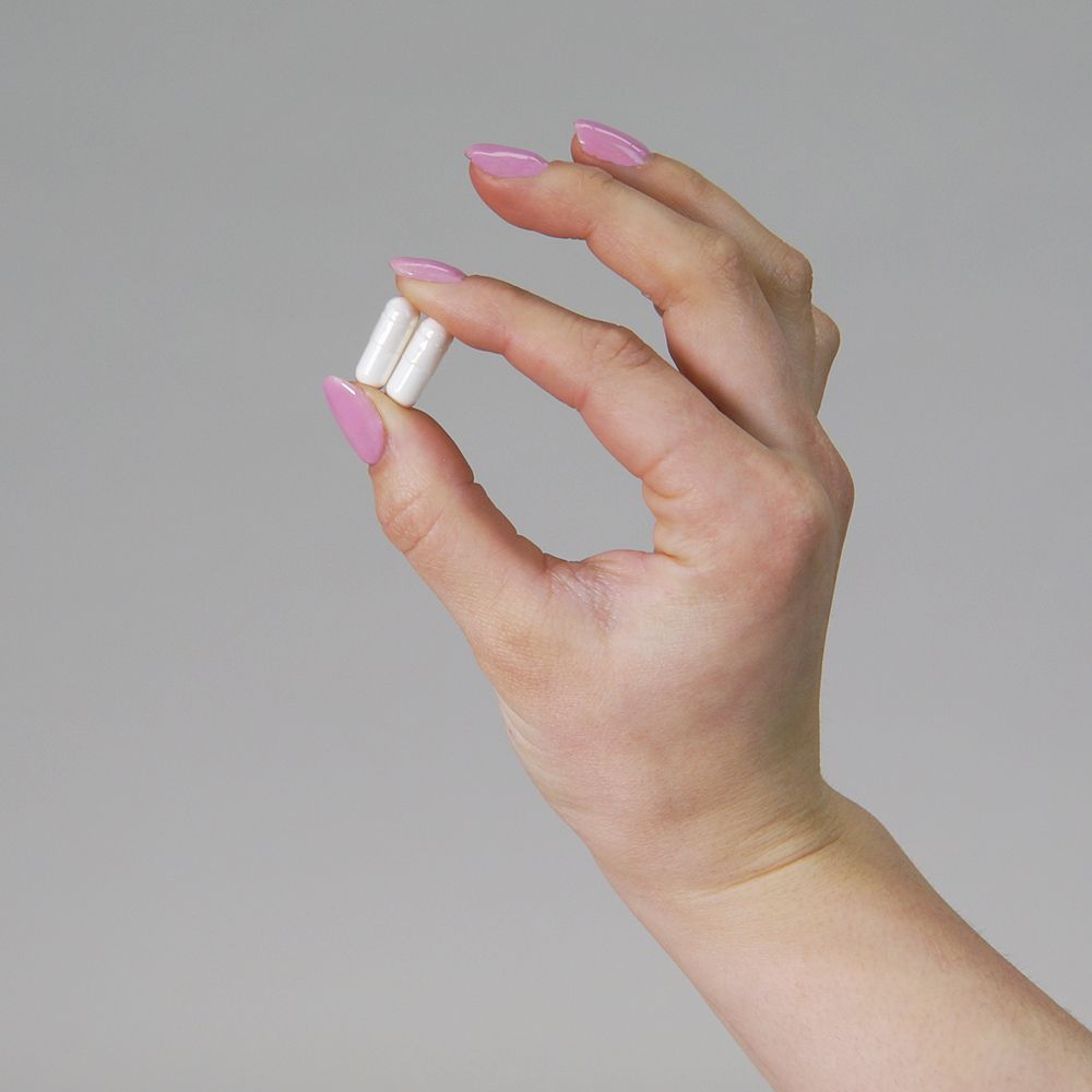 Mano che tiene due capsule bianche tra le dita. Unghie smaltate di rosa.