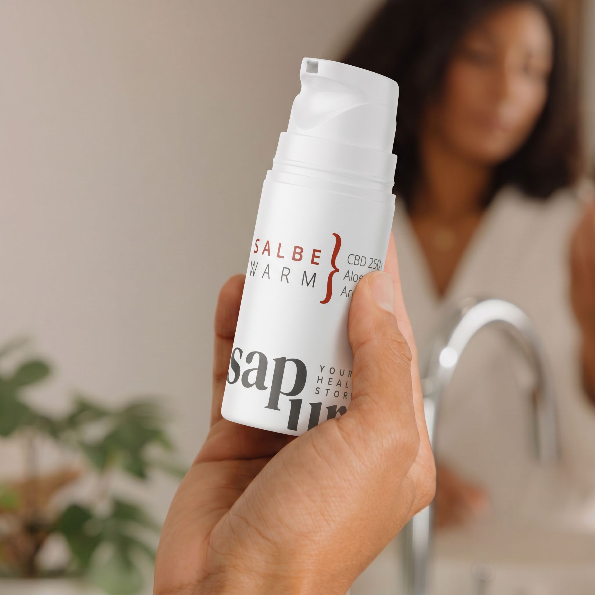 Mano che tiene un flacone di unguento bianco con CBD 250, Aloe Vera, Arnica. Specchio sullo sfondo.